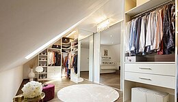Weißes Ankleidezimmer unter einer Dachschräge verbaut mit Schiebetüren als Raumteiler