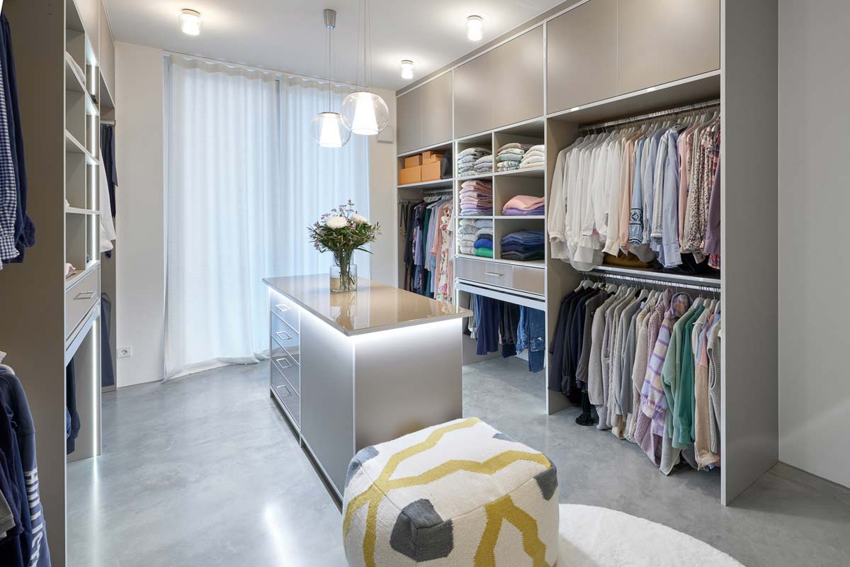 Ankleidezimmer in Taupe mit passender Insel, viel Beleuchtung sowie offenen und geschlossenen Elementen
